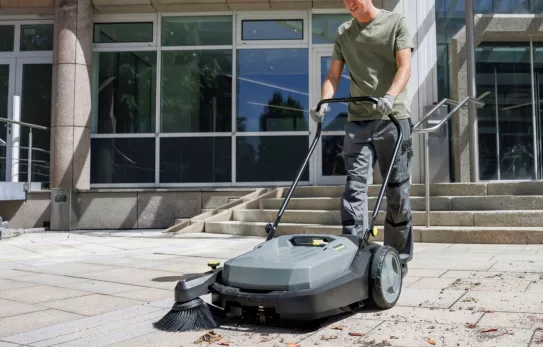 Medewerker reinigt een stoep met een veegmachine