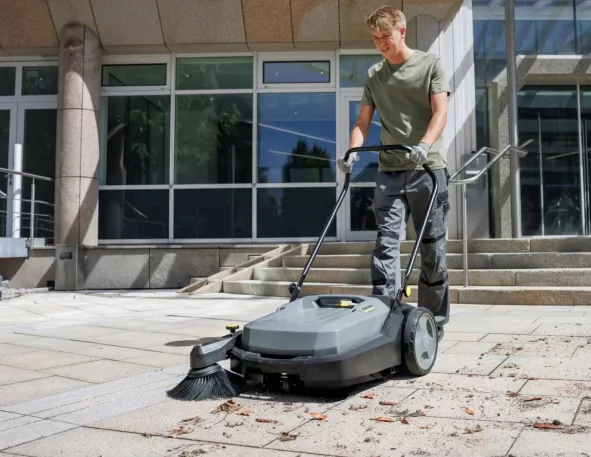 Medewerker reinigt een stoep met een veegmachine