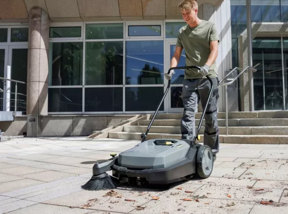 Medewerker reinigt een stoep met een veegmachine