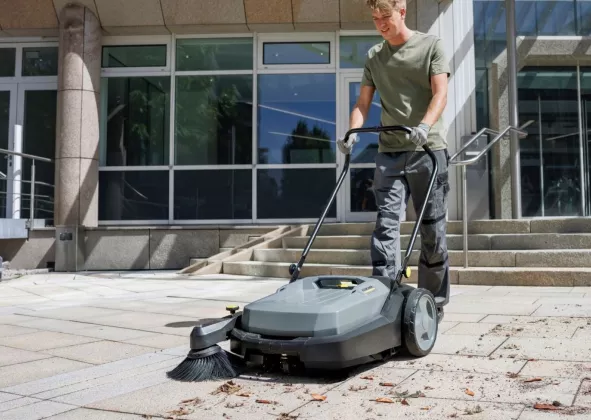 Medewerker reinigt een stoep met een veegmachine