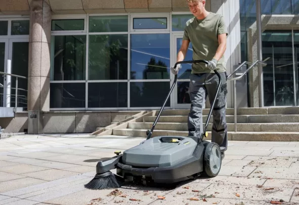 Medewerker reinigt een stoep met een veegmachine